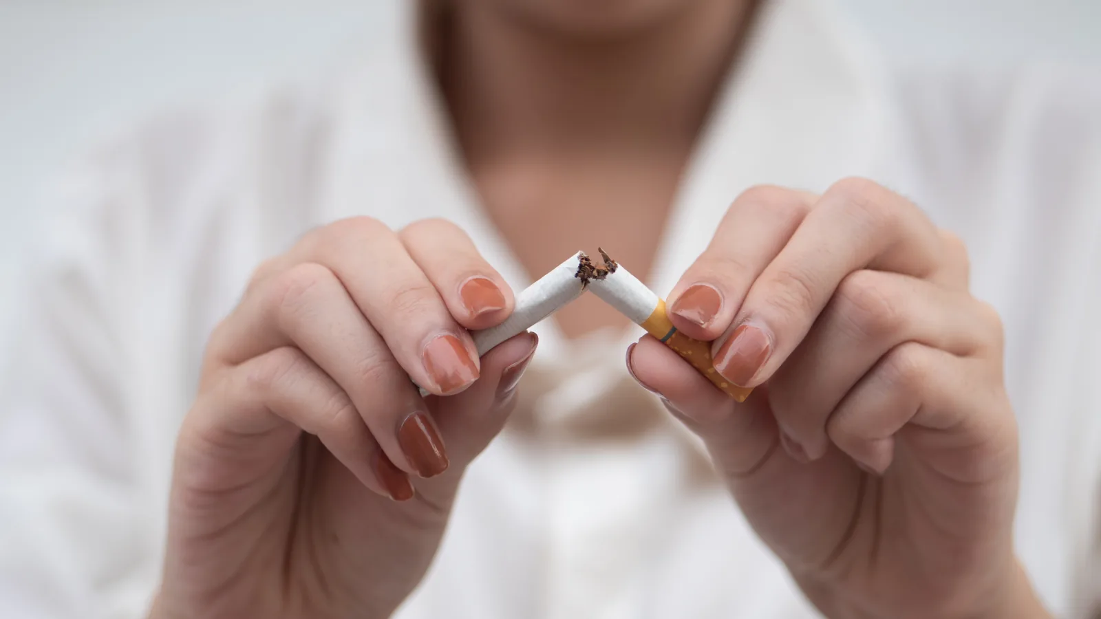 Mãos partindo um cigarro ao meio, em close, simbolizando a decisão de parar de fumar.